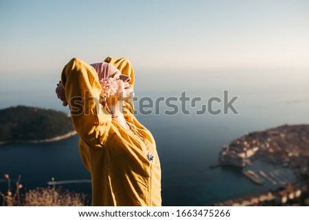 Woman with hijab standing above old city of Dubrovnik. She is happy and relaxed. She is enjoying sunset. 