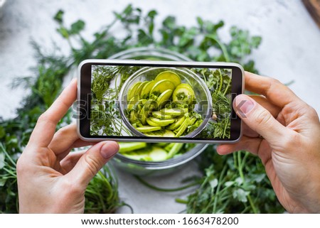 Make picture of food with phone. Hands hold smartphone. Photography of green fresh salad with zucchini. Vegan meal. Social media and blogging content style. 