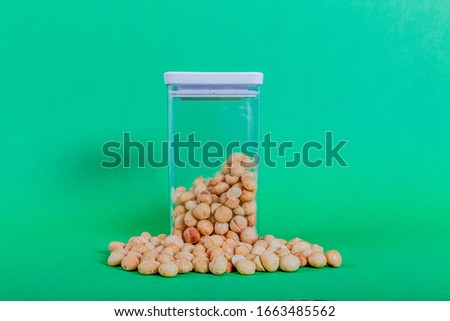 Macadamias outside and inside a transparent plastic container with a green background, also called Queensland, bush, maroochi, bauple, and Hawaii nut