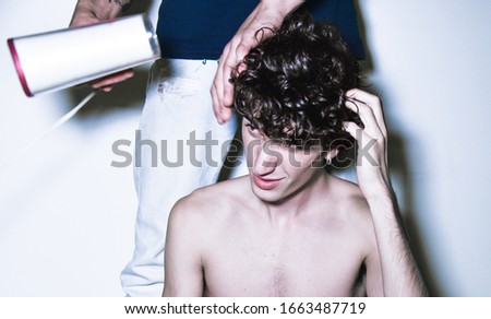 expressive mediterranean Italian
 dark haired handsome male boy model with angel face and fit sportive body posing for casual fashion shooting with hair dresser and hair blower