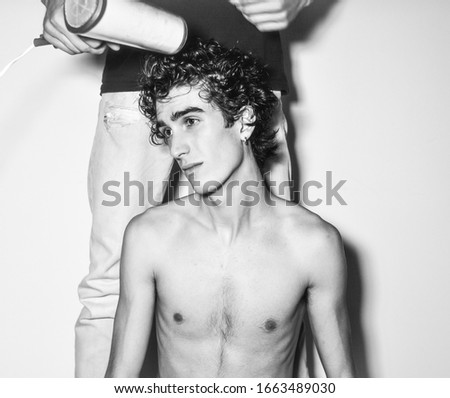 black and white. expressive mediterranean Italian
 dark haired handsome male boy model with angel face and fit sportive body posing for casual fashion shooting with hair dresser and hair blower