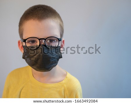 cute blonde boy in black medical mask and glasses is quarantined at home. child coughs heavily and wears mask. concept of fight against the coronavirus epidemic and proper prevention of infections