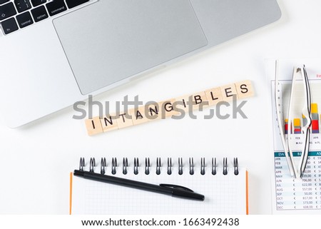 Intangibles concept with letters on wooden cubes. Still life of office workplace with supplies. Flat lay white surface with laptop computer and notepad. Intellectual capital and property. Royalty-Free Stock Photo #1663492438