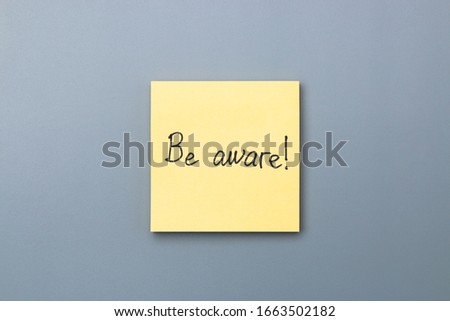 be aware on yellow sticky note over a grey background. april fools day