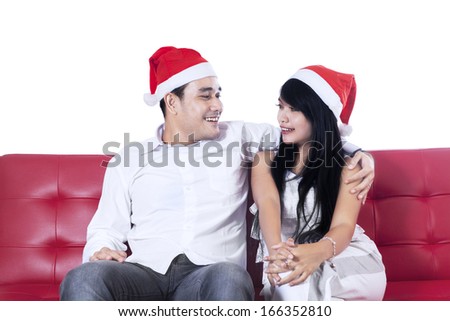Happy couple in christmas hats sitting on red sofa