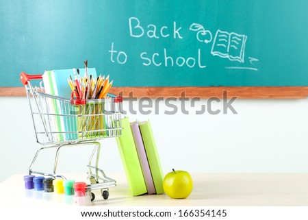School supplies in supermarket cart on blackboard background 