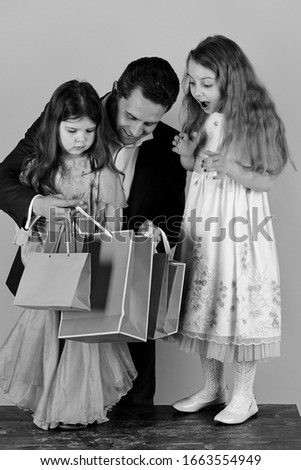 Schoolgirls and father hold pink packets looking inside. Girls and man with surprised faces hold shopping bags on pink background. Sisters and dad share presents. Shopping, presents and family concept