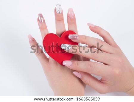 
Woman's hand with gel nails holding a red heart on white background. Health concept
