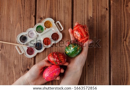 Close-up of woman's hands painting an easter egg on wooden background.
