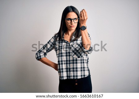 Young brunette woman with blue eyes wearing casual shirt and glasses over white background Doing Italian gesture with hand and fingers confident expression