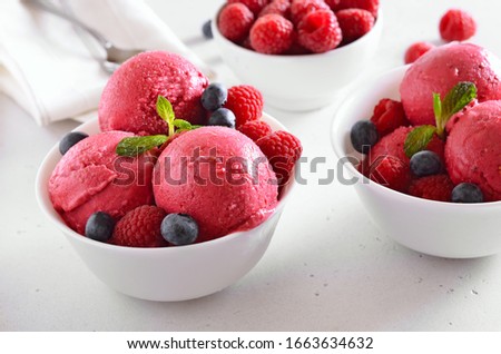Raspberry ice cream scoop with fresh raspberries and blueberries in bowl on stone background. Cold summer dessert. 