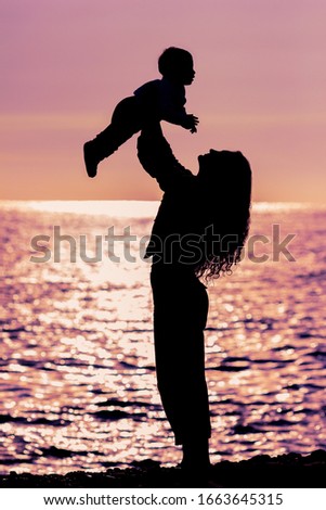 Silhouettes mom and baby at sunset. mother and little daughter play at sunset. Silhouette of mother throwing baby up on sunset