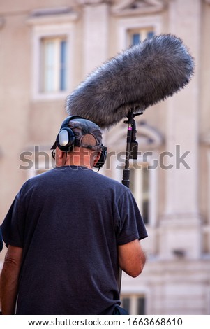 Behind the scene. Sound recorder with microphone, boom mic and headphones filming movie scene on outdoor location 