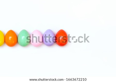 Top view of an Easter composition of painted eggs in bright juicy colors on a white background with a glossy texture. Holiday concept, flat layout, minimalism.