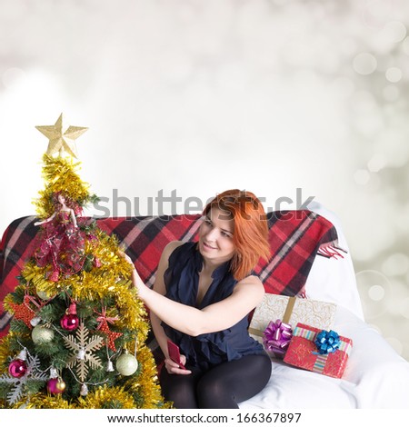 Happy red-haired woman on the sofa with a telephone and a gift box in Christmas holidays