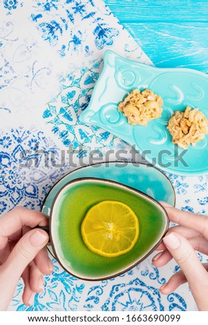 Female hand holding a turquoise cup of lemon tea. Top view, copy space