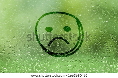 Sad unhappy face drawn on a fogged glass