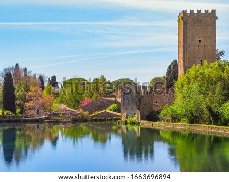 Botanical park, Garden of Ninfa or Giardino di Ninfa near the lake, with medieval castle ruins of Caetani family and various plants. Amazing scenery during spring. Beautiful landscape with blue sky.