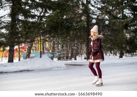 Young blonde girl in warm clothes skating in snowy winter park. Winter holidays concept