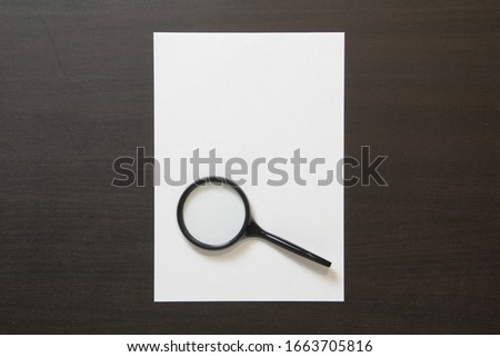 Template of white paper with magnefy on dark wenge color wooden background. Concept of searching, detecting and solving problems. Stock photo with empty space for text and design.