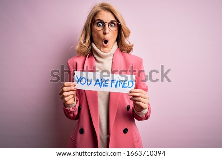 Middle age beautiful blonde business woman holding paper with you are fired message scared in shock with a surprise face, afraid and excited with fear expression