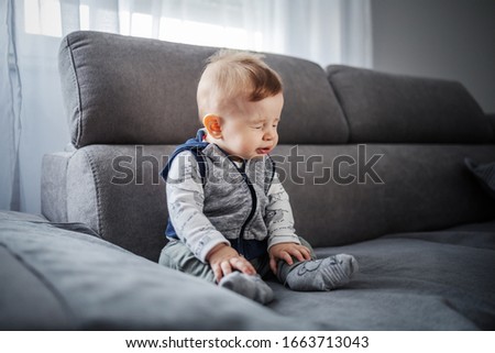 Adorable little boy sitting on couch in living room and sneezing. Royalty-Free Stock Photo #1663713043