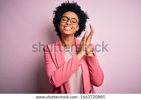Young beautiful African American afro businesswoman with curly hair wearing pink jacket clapping and applauding happy and joyful, smiling proud hands together Royalty-Free Stock Photo #1663720885
