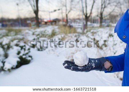 a hand in a black leather glove holds a snowball with a backdrop of a snowy field. the joy of winter and snow, a popular snow war game