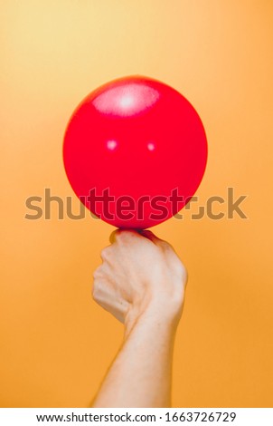 red balloon in womans hand on orange background