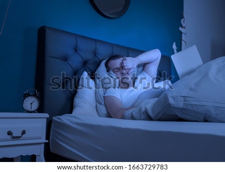 an overtired man works at late night on his laptop Royalty-Free Stock Photo #1663729783