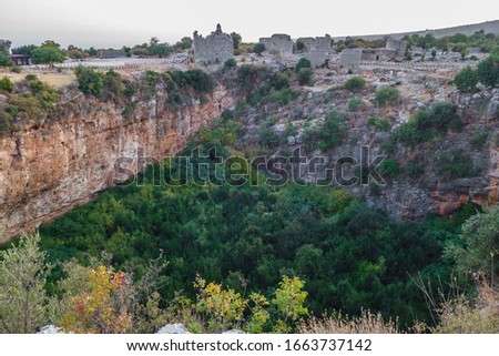 Panoramic view onto ruins of buildings, standing near edge of karst sinkhole in ancient city Kanli Divane or Canytelis, Ayaş, Turkey. There are remains of churches  tower. Photo taken in evening