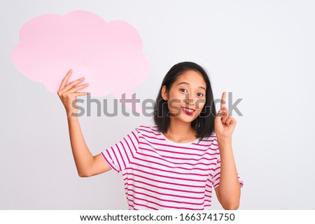 Young chinese woman holding cloud speech bubble standing over isolated white background surprised with an idea or question pointing finger with happy face, number one