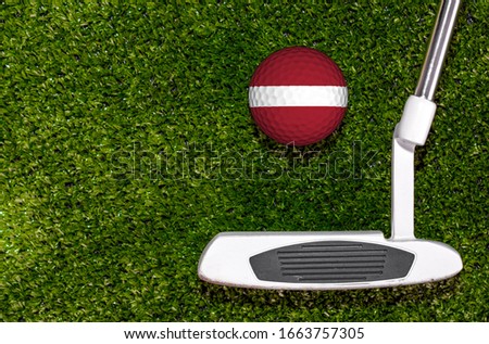 A golf club and a ball with flag Latvian during a golf game.