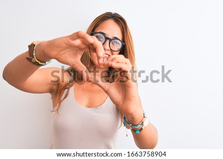 Young redhead woman wearing glasses standing over white isolated background smiling in love showing heart symbol and shape with hands. Romantic concept.