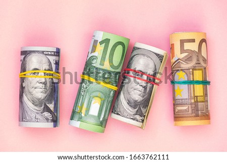 rolls of 100 dollar, 50 and 100 euro banknotes on pink background