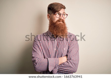 Handsome Irish redhead business man with beard wearing glasses over isolated background smiling looking to the side and staring away thinking.