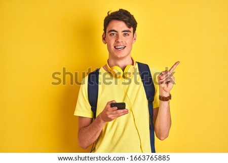 Teenager boy wearing headphones and using smartphone over isolated background very happy pointing with hand and finger to the side