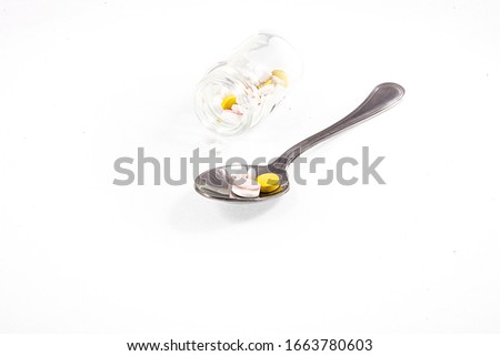a small glass container and a silver spoon with medicine on a white isolated background