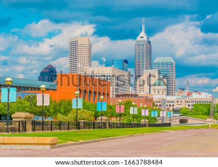 A brick walkway leads through the White River State Park and past the Indianapolis skyline, including the capitol building.
