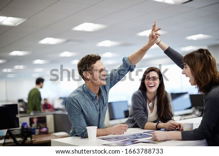 Three people in an office looking at photographs and making a high five gesture. Royalty-Free Stock Photo #1663788733