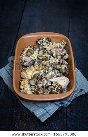 Baked chicken with mushrooms and cheese in a ceramic baking dish on a dark wooden background. In a simple rustic style. Selective flus, blur.