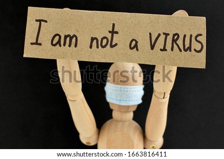 Cardboard sign with text I am not a virus in the hands of a wooden doll or mannequin in a medical mask. Concept of anti racism, anti xenophobia, the social situation around the Coronavirus or Covid-19
