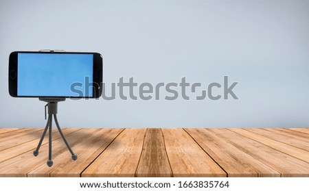 
A studio shot of a cellphone on a tripod isolated  on a empty room with wooden floor and solid blue  color wall mockup background.