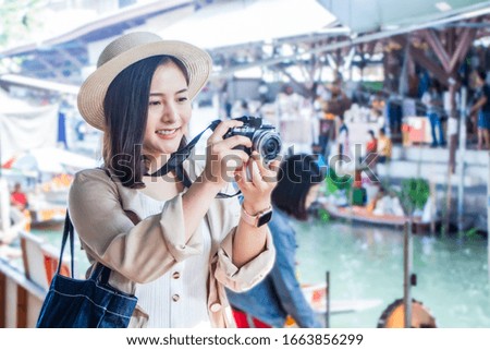 asia female tourists wearing hat holding camera and smartphone take photo vlog live . Beautiful woman visiting Damnoen Saduak floating market,Ratchaburi.