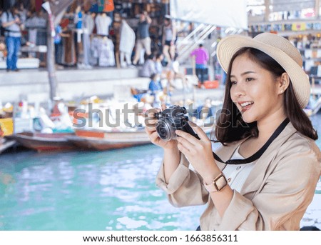 asia female tourists wearing hat holding camera and smartphone take photo with floating market background copy space . Beautiful woman smiling teeth visiting Damnoen Saduak floating market,Ratchaburi.