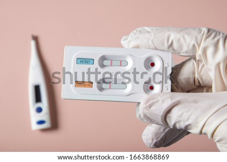 Doctor holding a test kit for viral diseases H1N1 flu and COVID-19 2019-nCoV. Lab card kit tested NEGATIVE for viral novel coronavirus sars-cov-2 virus and POSITIVE for H1N1 Royalty-Free Stock Photo #1663868869