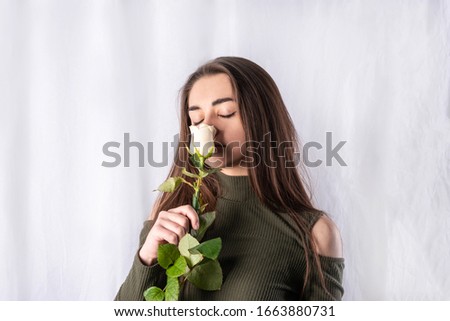 Portrait of a young beautiful girl.  She is holding a rose.  She closed her eyes and enjoys the scent of a rose.  Studio shooting, on a white sheet Royalty-Free Stock Photo #1663880731