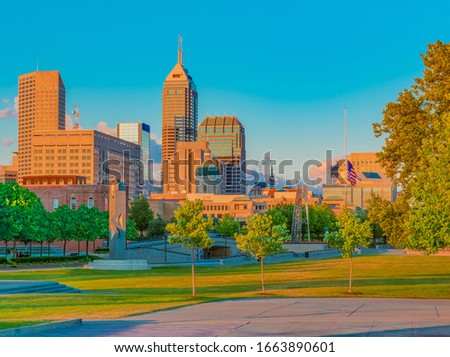 Late afternoon light hits the buildings in the skyline of Indianapolis, Indiana, from the White River State Park. The grass, trees and capitol building glow in the light.