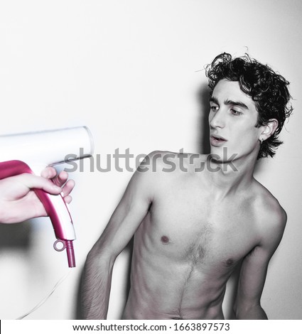 expressive mediterranean Italian dark haired handsome male boy model with angel face and fit sportive body posing for casual shooting playing with hair blower