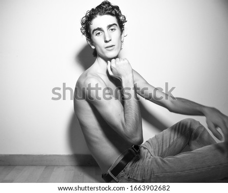 black and white expressive mediterranean Italian dark haired handsome male model boy with angel face and fit sportive body posing for casual fashion shooting lying on wooden floor wearing  jeans